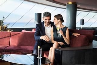 A couple enjoys a refreshing drink together in the luxurious Top Sail Lounge with panoramic sea views | MSC Cruises