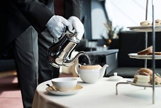 A dedicated crew member serves tea and pastries in the elegant Top Sail Lounge of the MSC Yacht Club | MSC Cruises