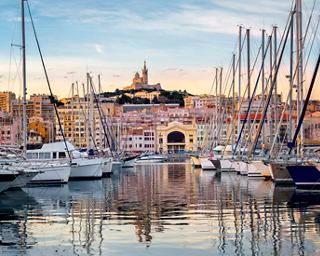 A serene marina in Marseille with boats gently bobbing in the water, featuring the iconic Notre-Dame de la Garde in the background | MSC Cruises