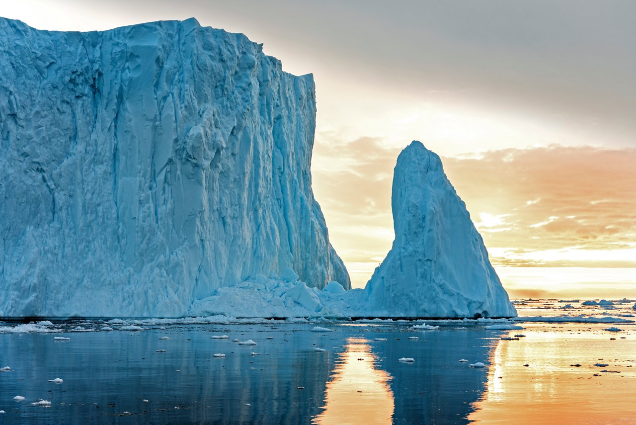 An impressive iceberg reflects in the calm waters under a soft sunset in Greenland | MSC Cruises