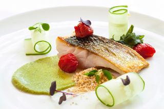 A beautifully plated grilled sea bass fillet garnished with tomatoes, avocado sauce, and fresh vegetables | MSC Cruises