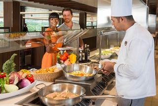 A chef prepares a delicious meal at the Marketplace Buffet while a couple enjoys the vibrant atmosphere on board | MSC Cruises