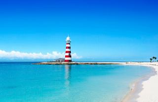 Una scena di spiaggia tranquilla con un faro rosso vicino al mare turchese sotto un cielo blu chiaro | MSC Crociere