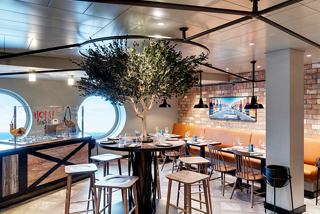 A stylish dining area showcasing the Hola! Tapas Bar by Ramon Freixa with a tree, portholes and inviting tables | MSC Cruises