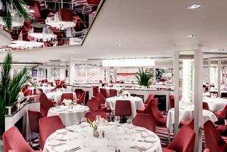 The elegant dining area of the main restaurant on MSC Grandiosa, featuring stylish red decor and round tables | MSC Cruises