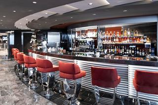 A stylish bar counter with red stools invites relaxation in the elegant Top Sail Lounge of MSC Grandiosa | MSC Cruises
