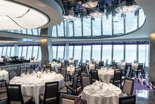 Elegant dining area with tables set against panoramic windows, offering stunning sea views aboard MSC Grandiosa | MSC Cruises