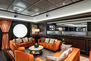 A comfortable seating area in L'Atelier Bistrot featuring warm orange sofas and a large porthole | MSC Cruises