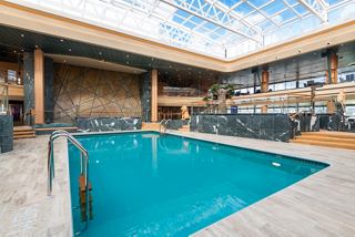A serene indoor pool area with a sliding roof, surrounded by elegant wooden features and ample seating | MSC Cruises