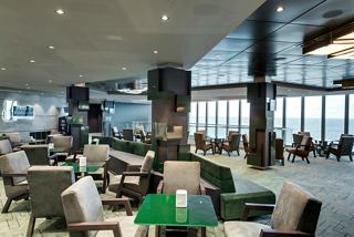 Elegant seating area with tables and large windows offering views of the sea at the Edge Cocktail Bar | MSC Cruises