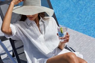 A woman relaxing by the pool, enjoying a soft drink under a wide-brimmed hat | MSC Cruises