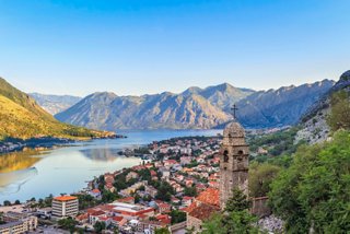 A panoramic view of Kotor's bay at sunrise, surrounded by majestic mountains and scenic buildings | MSC Cruises