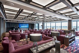 A stylish lounge area with plush seating, large windows, and a stage for entertainment on the MSC Seaview | MSC Cruises