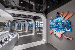 A modern corridor with stylish decor leading to The Piazza and a vibrant sports bar sign | MSC Cruises