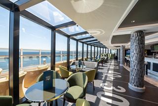 A spacious lounge area with seating and a bar, offering stunning sea views through large windows | MSC Cruises