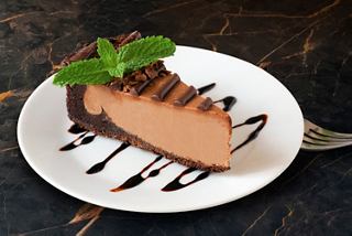 A slice of chocolate cheesecake garnished with mint leaves on a white plate with chocolate drizzle | MSC Cruises