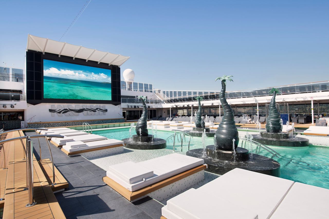 A serene pool area with sun loungers and a large LED screen surrounded by clear skies | MSC Cruises