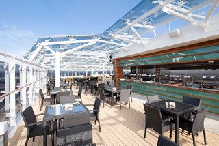 A stylish outdoor dining area with tables and chairs, offering a stunning view for guests at the MSC Yacht Club Grill & Bar | MSC Cruises