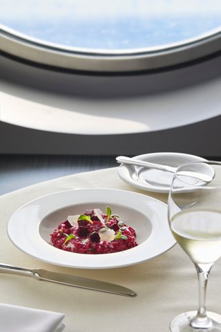A beautifully presented bowl of risotto paired with a glass of wine, set against a scenic porthole view | MSC Cruises
