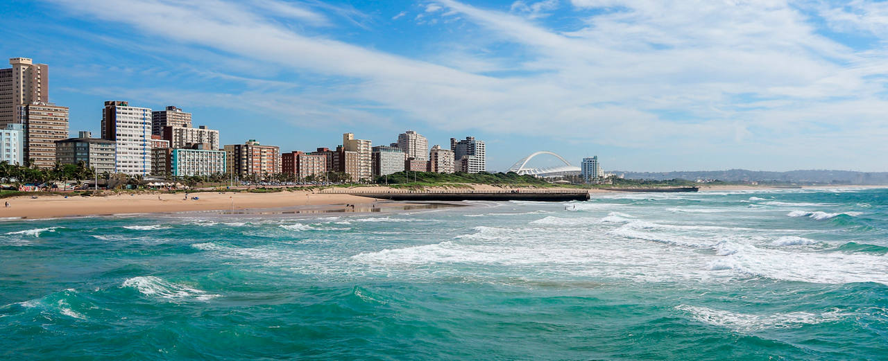 Ein malerischer Blick auf die Küste von Durban mit Wellen, die am Strand brechen, und Gebäuden entlang des Ufers | MSC Cruises