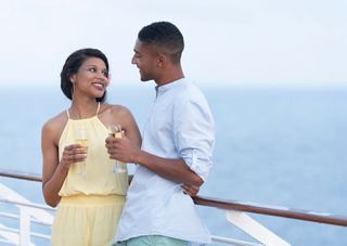 A couple enjoying a moment together on a cruise, with drinks in hand, overlooking the sea from the ship's balustrade | MSC Cruises