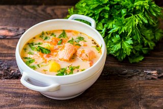 A bowl of traditional Finnish Lohikeitto soup with salmon, cream, and herbs, accompanied by fresh greens | MSC Cruises