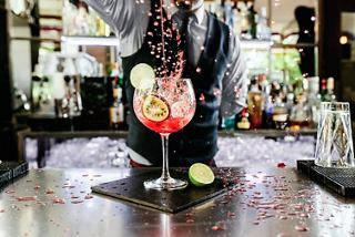 A bartender prepares a vibrant cocktail garnished with fresh fruit at a stylish bar counter | MSC Cruises