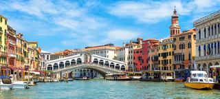 Eine malerische Aussicht auf den Canal Grande in Venedig mit bunten Gebäuden und der ikonischen Rialtobrücke im Hintergrund | MSC Cruises