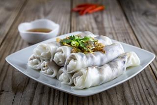 A plate of steamed rice noodle rolls garnished with herbs and served with a dipping sauce | MSC Cruises