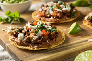Deliciosos tacos con carne de res, tomate, queso y hierbas frescas, servidos con lima en una tabla de madera | MSC Cruceros