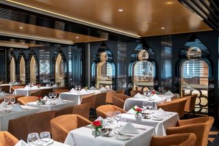 An elegant restaurant setting with tables adorned with flowers and a view of the promenade | MSC Cruises