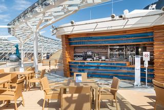 A vibrant bar area with wooden seating and a stylish counter, inviting relaxation and socialising under a bright sky | MSC Cruises