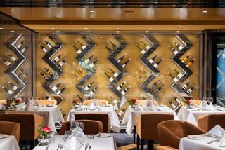 Elegant dining setup at Il Campo Restaurant, featuring tables adorned with flowers against a vibrant patterned wall | MSC Cruises