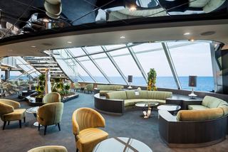 A stylish lounge area in the MSC Yacht Club features large windows with sea views, inviting seating, and elegant decor | MSC Cruises