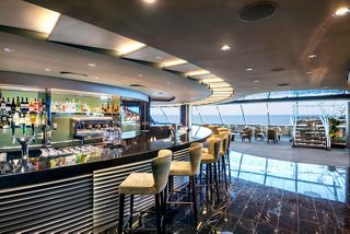 A stylish lounge area featuring a bar counter and comfortable seating in the MSC Yacht Club on MSC Virtuosa | MSC Cruises