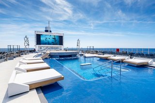 La acogedora piscina Long Island en el MSC Seashore, rodeada de tumbonas y un cielo azul claro | MSC Cruceros