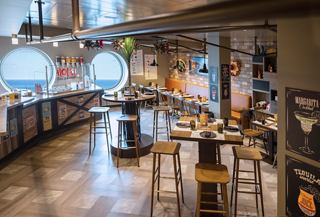 A welcoming dining area with tables and porthole views, perfect for enjoying meals at Hola! Tacos & Cantina | MSC Cruises