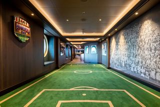 A vibrant sports bar corridor featuring green turf, portholes, and warm lighting, inviting guests to enjoy the experience | MSC Cruises