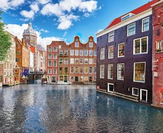 Charming canal-side houses reflect in the water under a bright blue sky in a picturesque Dutch setting | MSC Cruises