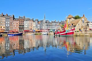 Des maisons pittoresques et des bateaux se reflètent dans les eaux sereines du port d'Honfleur, capturant le charme de la vie côtière française | MSC Cruises