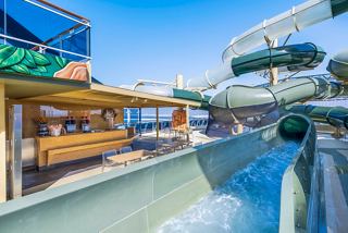 A vibrant outdoor area on MSC Virtuosa featuring a waterslide, seating, and a lively bar atmosphere | MSC Cruises