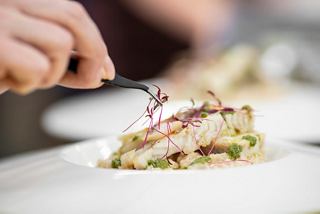 A hand delicately plating a gourmet fish dish with fresh ingredients | MSC Cruises