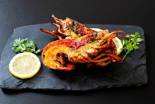 Langostas y cangrejos a la parrilla, decorados con limón y salsa en una bandeja de pizarra | MSC Cruceros