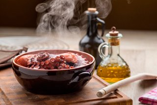 Un plato caliente de pulpo en una tabla de cortar con aceite de oliva y especias, evocando una deliciosa experiencia culinaria | MSC Cruceros