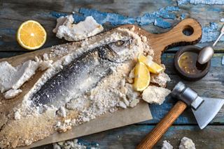 Lubina fresca preparada con sal, especias y limón sobre una tabla de madera lista para hornear | MSC Cruceros