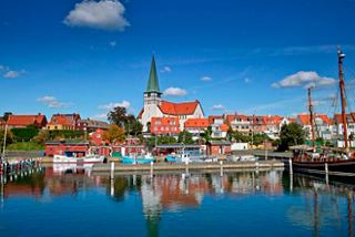 Un port pittoresque à Ronne, Danemark, avec des bateaux colorés et un charmant clocher sous un ciel bleu clair | MSC Croisières