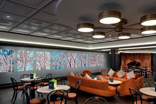 The vibrant seating area of L'Atelier Bistrot featuring a striking art wall and inviting table arrangements | MSC Cruises