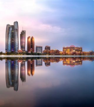 Abu Dhabi skyline reflecting on the water at sunset, showcasing modern architecture and coastal beauty | MSC Cruises