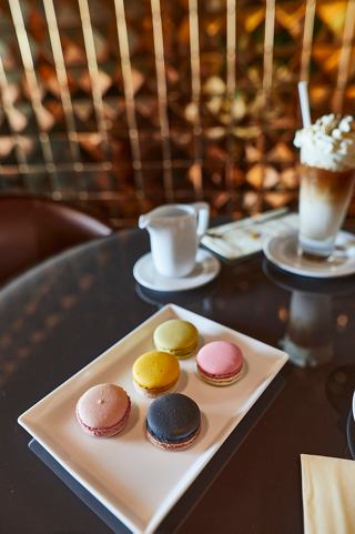 A delightful selection of colourful macarons on a wooden platter beside a coffee drink and whipped cream | MSC Cruises