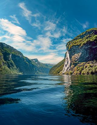 Una vista serena del fiordo de Geiranger, con montañas exuberantes y aguas tranquilas bajo un cielo brillante | MSC Cruceros